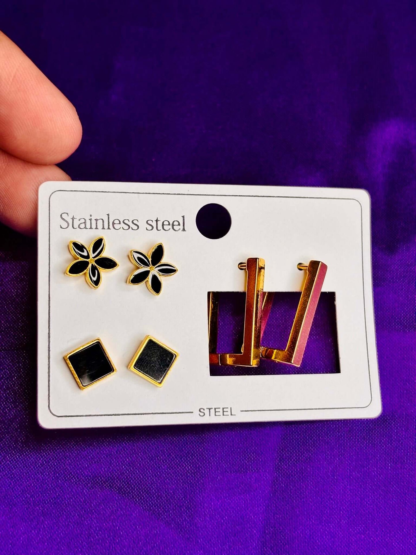 Stainless steel black and gold earring set of 3, including floral stud, square, and rectangular designs. Imitation jewelry.